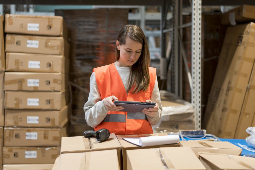Employée en gilet de sécurité utilisant une tablette dans un entrepôt, symbolisant la gestion des stocks et l'optimisation logistique avec un ERP.