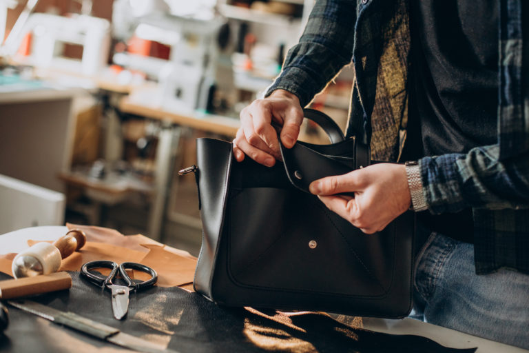 Artisan en atelier optimisant la production de maroquinerie avec des outils de précision.