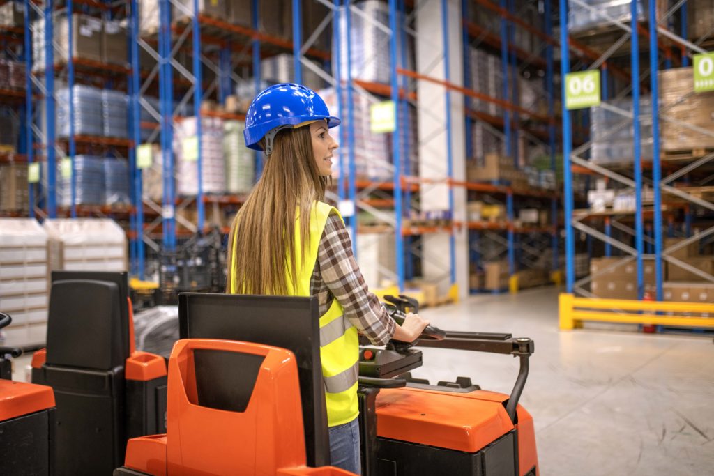 Opératrice logistique conduisant un chariot élévateur dans un entrepôt, illustrant la fluidité des flux internes et l’organisation des stocks