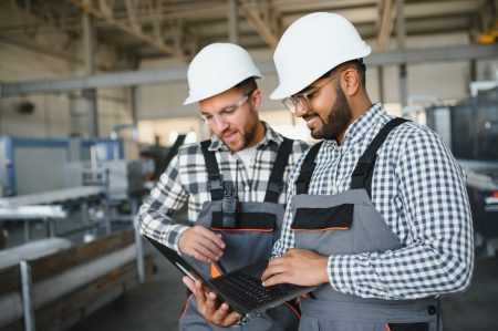 Two male international workers in overalls work together at a machine for the production of aluminum PVC windows and doors Gestion et suivi automatisé des ressources humaines par l'ERP d'Open-Prod dans une industrie
